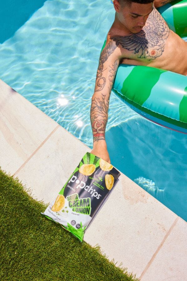 Person in a pool reaching for a bag of Popchips