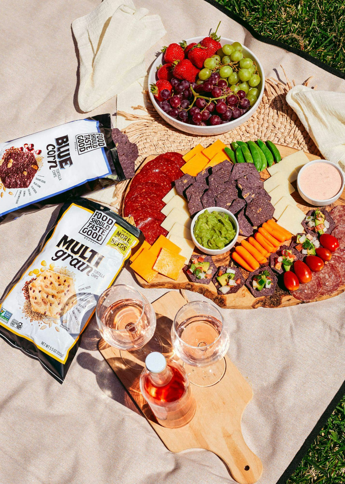 Picnic blanket with chips, charcuterie board, and drinks.