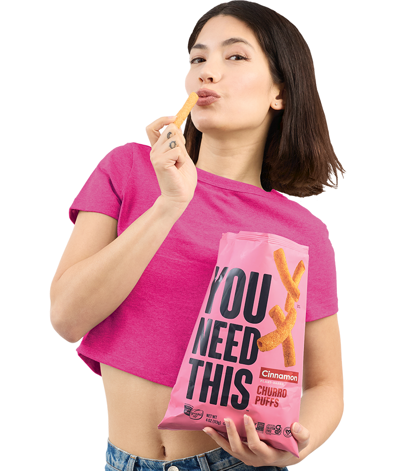 Person in a pink shirt holding a "You Need This" chip bag and eating chips.